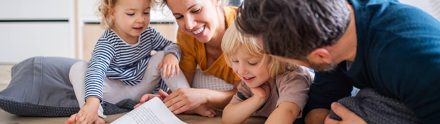 A family with two kids reading a book on the floor.